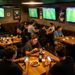 Kết quả bóng đá updates during a lively sports betting night at a bar with fans cheering