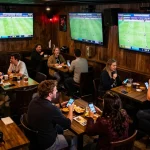 Enthusiastic fans engaging in sports betting, analyzing tỷ lệ cá cược bóng đá with excitement during live matches.